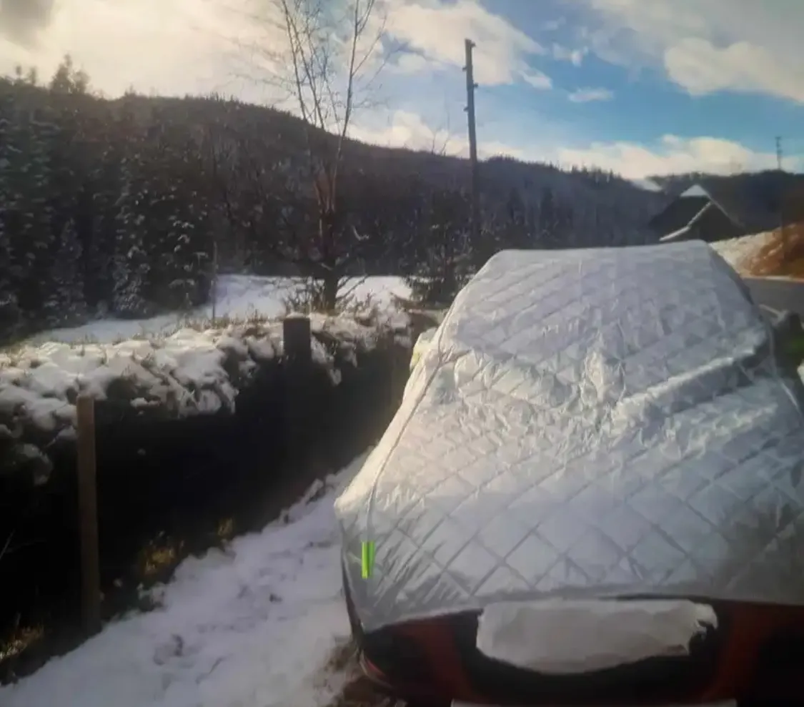 Auto coperta dal telo in montagna con neve